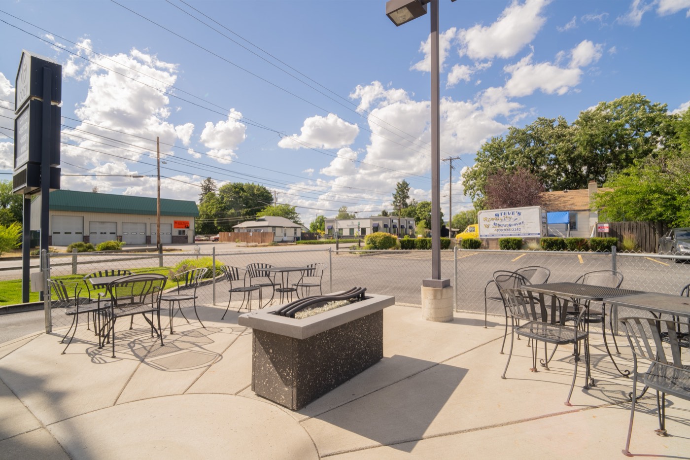 The Cozy Coffee patio with wrought-iron tables around a gas fire pit on a sunny day